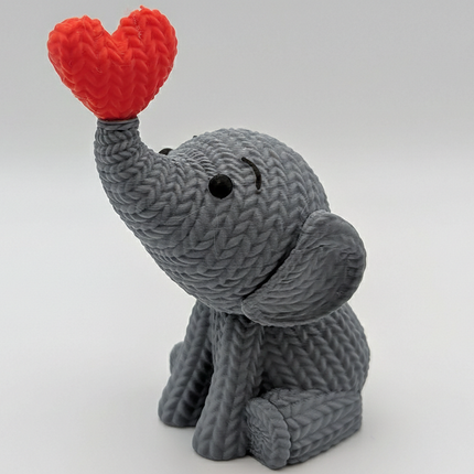 „Meilės drambliukas“ – Megztos tekstūros skulptūra su raudona širdimi